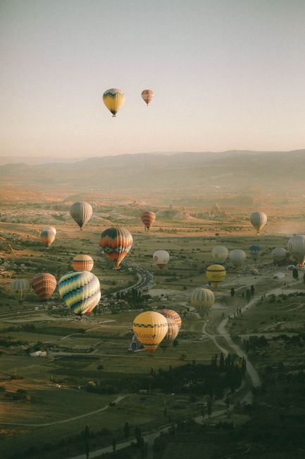 Beautiful aerial view of hot air balloons floating over Cappadocia's unique landscape at sunset.