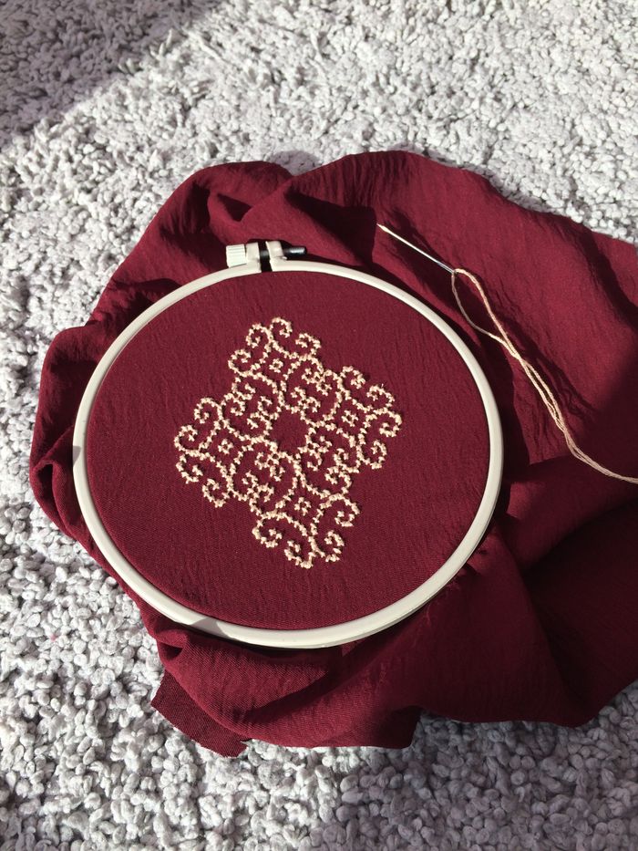Cross-stitch pattern on maroon fabric in an embroidery hoop