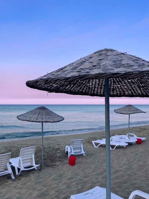 Free Peaceful beach with straw umbrellas and loungers at sunset, perfect for relaxation. Stock Photo