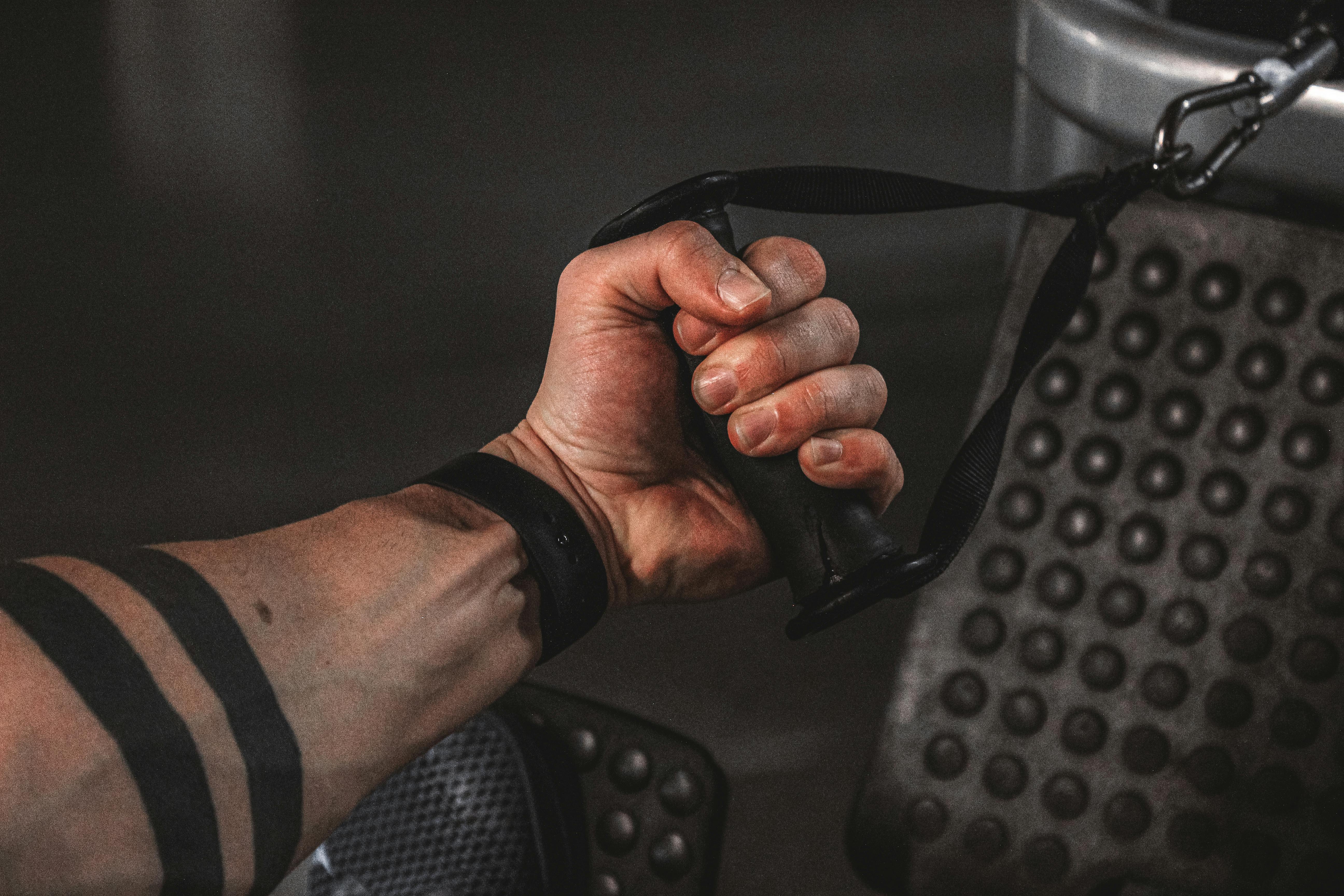 Close-up of a male hand gripping gym cable, showcasing strength and arm tattoo.