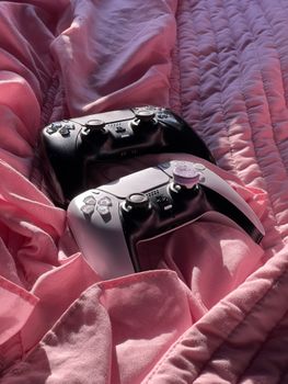 Two gaming controllers resting on a pink duvet cover, capturing a cozy gaming ambiance.