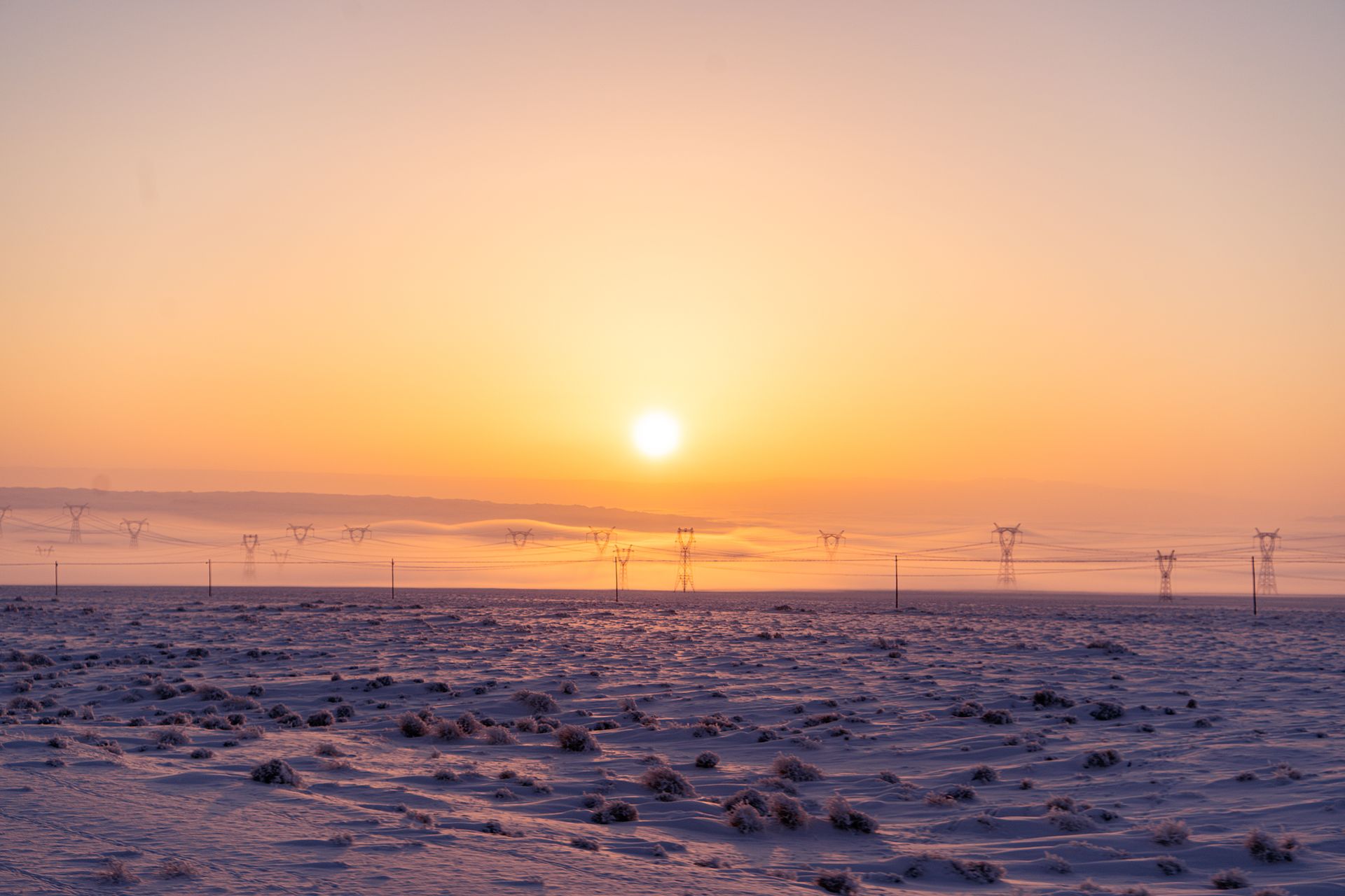 Tranquil sunset in Xinjiang's snowy desert with power lines and serene landscape.
