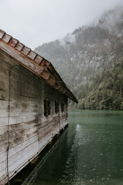 Scenic view of a rustic cabin by a misty lake surrounded by foggy forested mountains.
