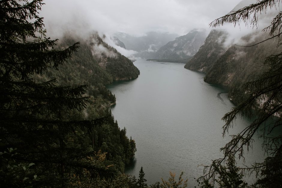 Scenic aerial view of a serene lake surrounded by misty mountains and dense forest.