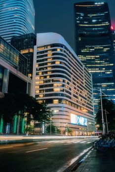 Dramatic view of illuminated skyscrapers at night with light trails on city street.