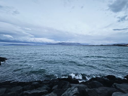 Free Dramatic seascape of Iceland's rugged coastline with distant mountains under a cloudy sky. Stock Photo