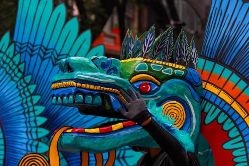 A Person Wearing Blue, Green and Yellow Dragon Head During a Parade