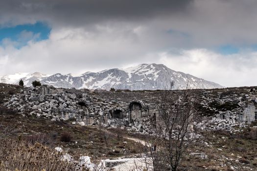 Explore the timeless beauty of ancient ruins set against a backdrop of majestic snowy mountains and a dramatic sky.