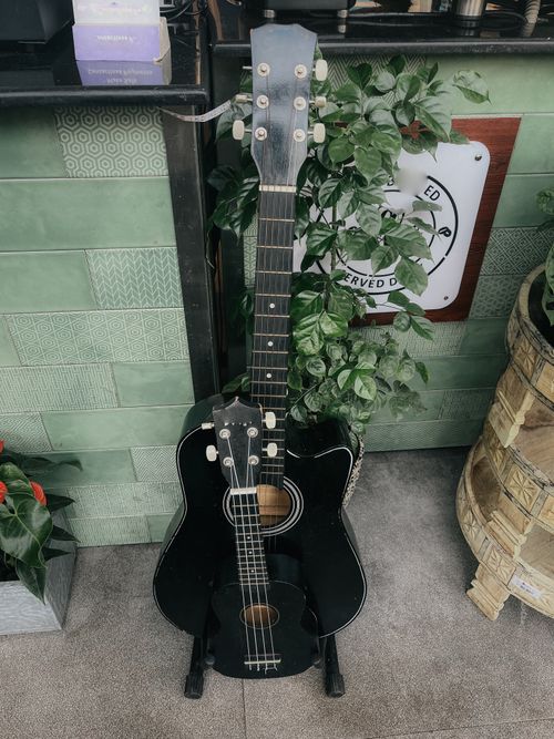 Free Acoustic guitar and ukulele leaning against a wall with green tiles and plants. Stock Photo