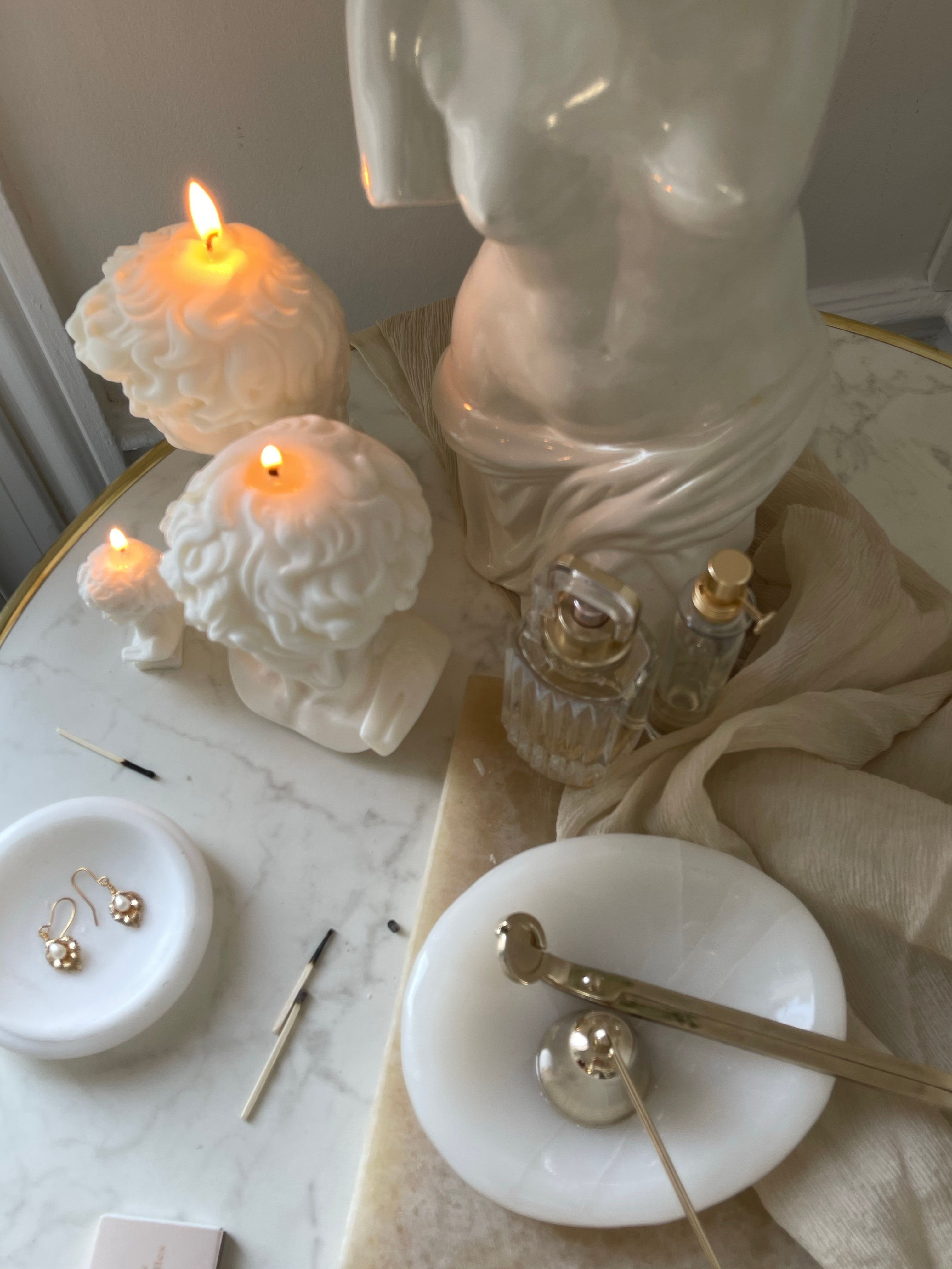 Artistic candlelit still life on marble with sculptures and glass decor.