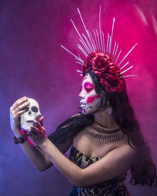 Free A woman with painted face and colorful attire celebrates Dia de Muertos, holding a skull with a vibrant background. Stock Photo