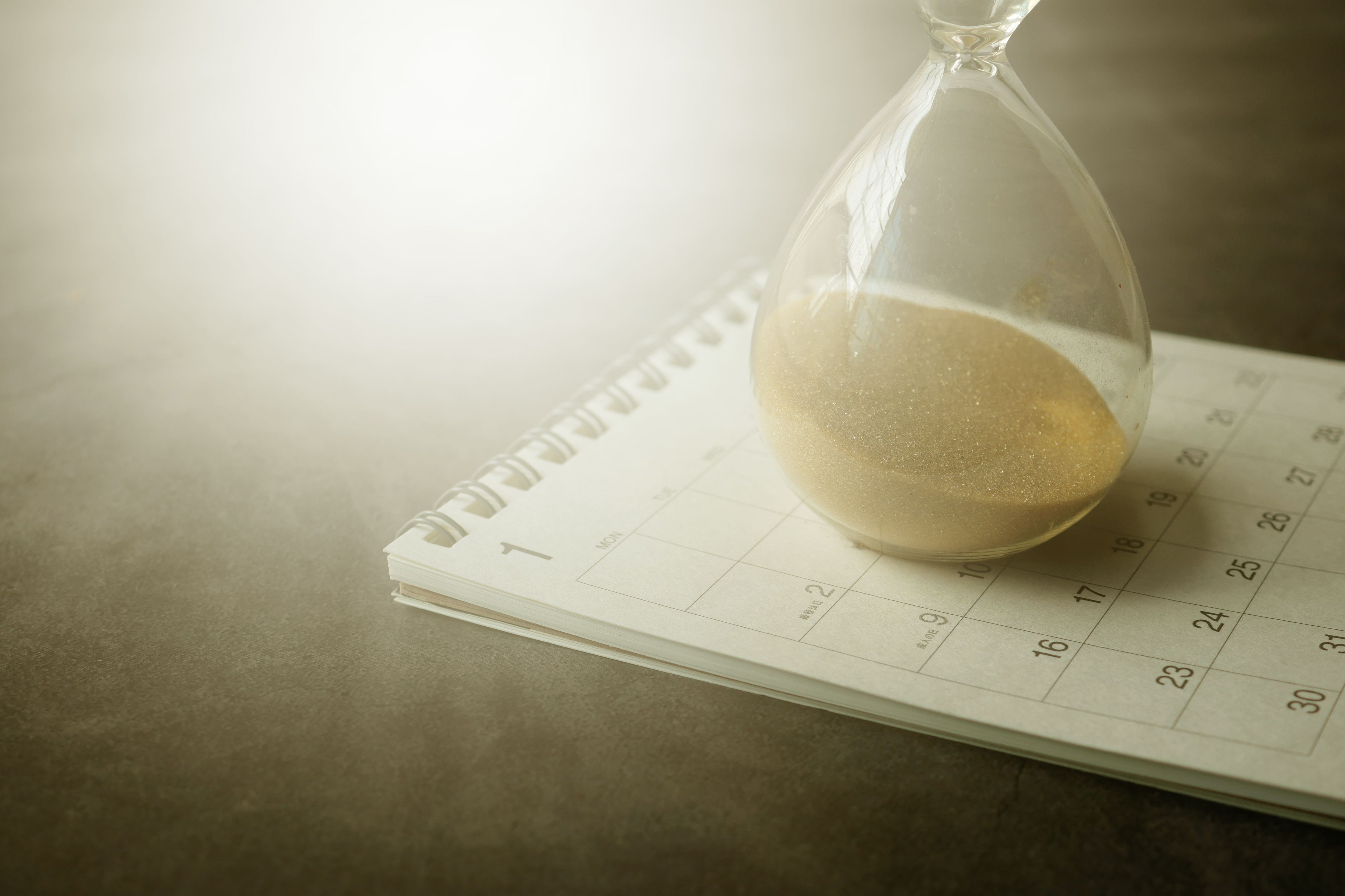 Hourglass resting on a calendar, symbolising time passing and an approaching deadline