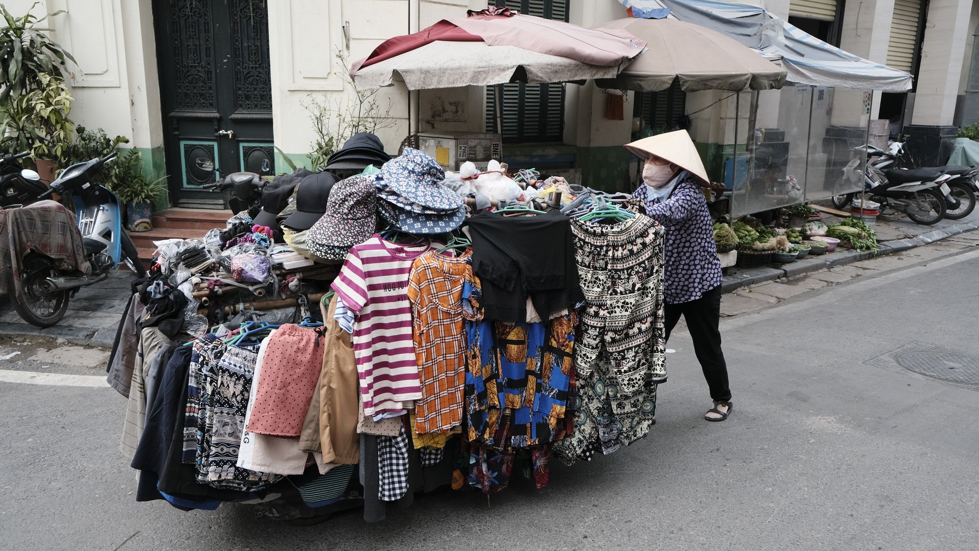 A bustling street vendor displays diverse clothing under umbrellas in a vibrant urban market.