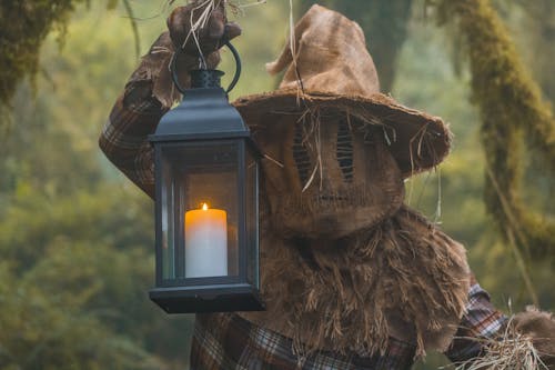Person Dressed in a Scarecrow Halloween Costume Holding a Lantern in a Forest 