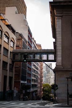 View of an urban street featuring a skybridge connecting buildings in a dense cityscape.