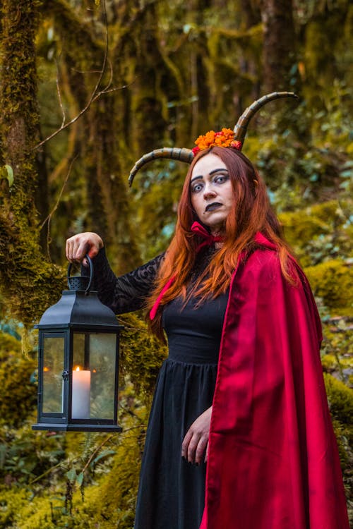 Woman Wearing a Halloween Costume with Red Cape and Horns Posing in a Forest 
