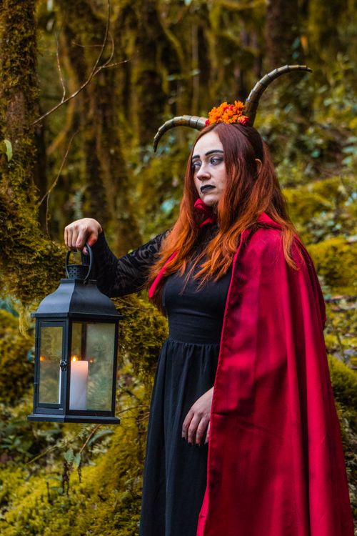Free A woman in a red cape with horns holds a lantern in an enchanted forest. Stock Photo