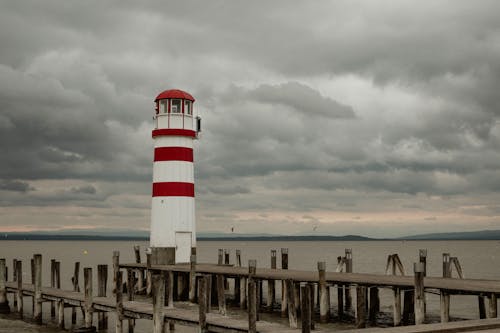 White and Red Lighthouse on Wooden Dock under the Cloudy Sky