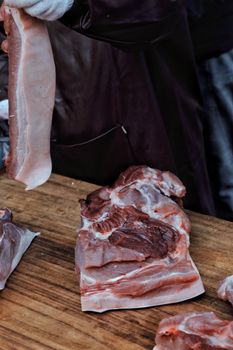 Close-up of raw pork meat being processed by butcher on wooden board for culinary preparation.