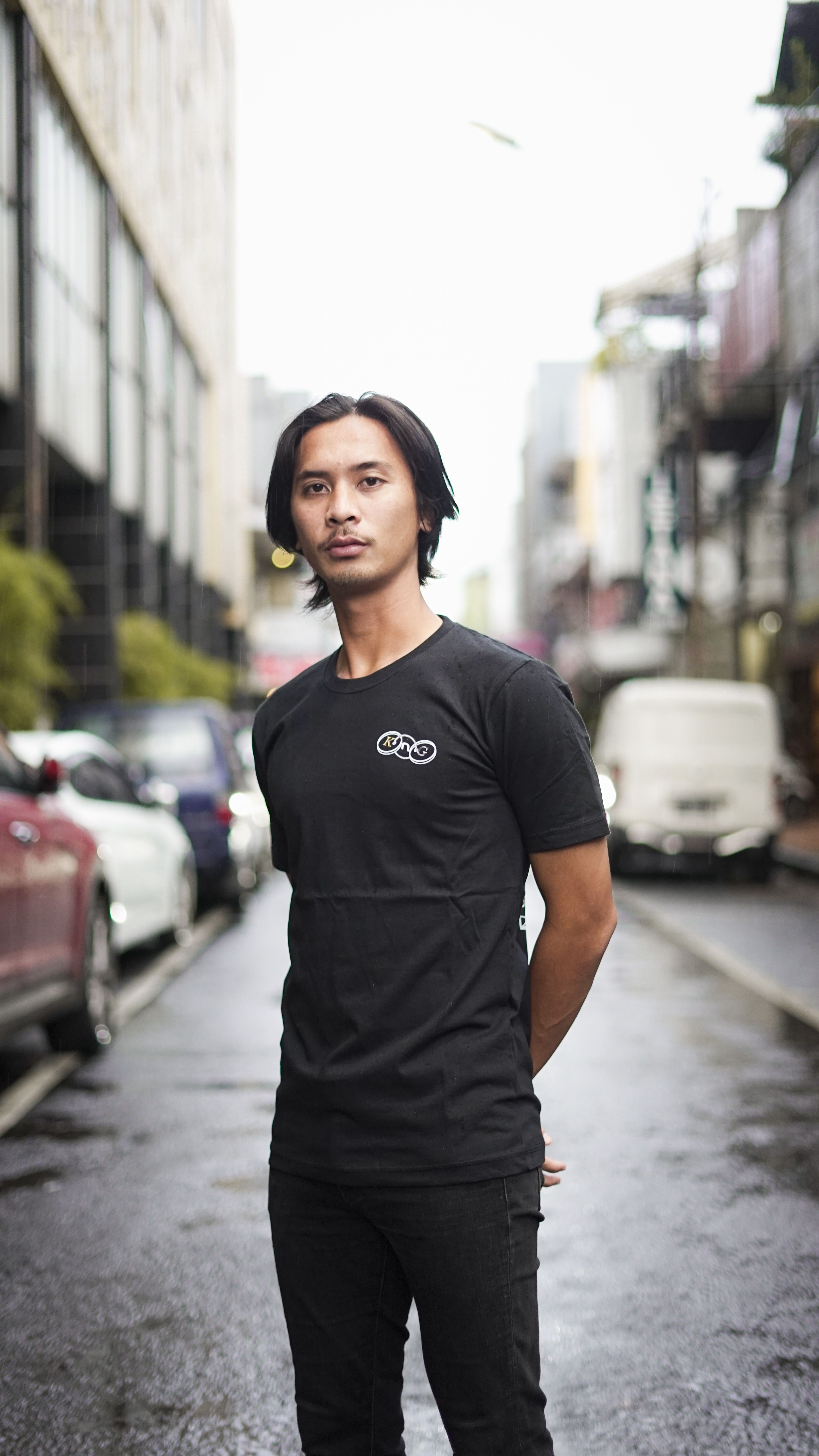Fashionable young man in black attire posing confidently on city street.