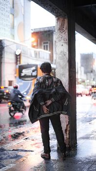 A man stands in the rain observing city traffic. An urban, atmospheric street view. - Fotografer Sidoarjo