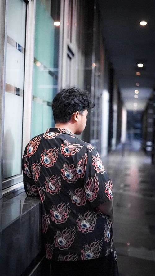 Free A man in a printed shirt stands in a modern indoor hallway, captured from behind. Stock Photo
