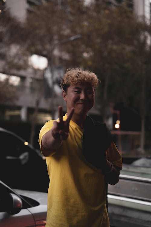A Man in Yellow Shirt Smiling while Doing Peace Sign