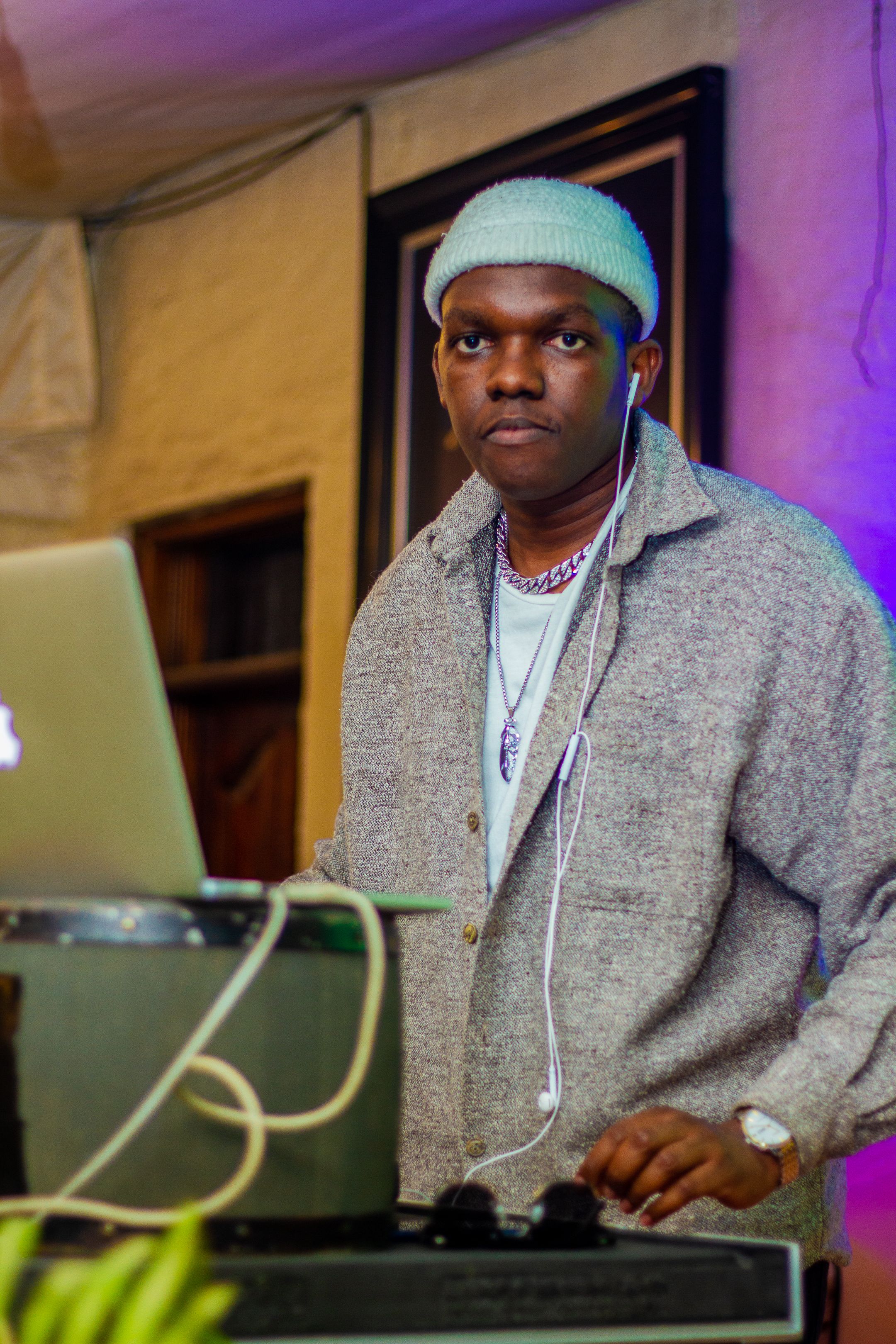 DJ wearing a beanie and earphones mixes music at an indoor event in Nairobi, Kenya. Vibrant and lively atmosphere.