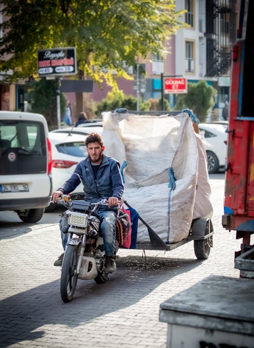 Man Driving Motorcycle with Loaded Trailer on Sidewalk