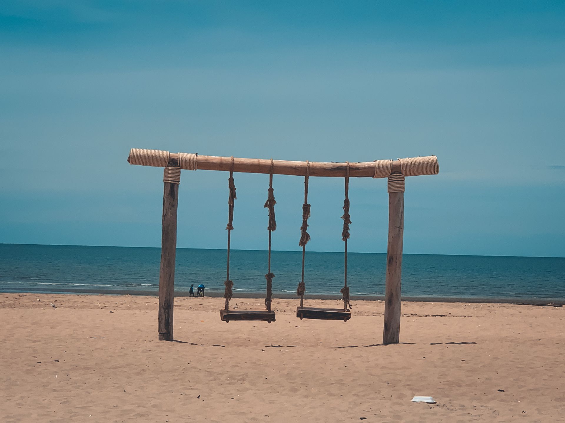 Rustic wooden swing set on a serene beach in Cha-am, Thailand, under a clear blue sky.