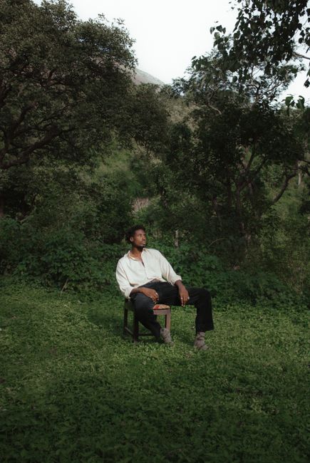 A man in casual attire sits on a chair in a serene green forest environment.