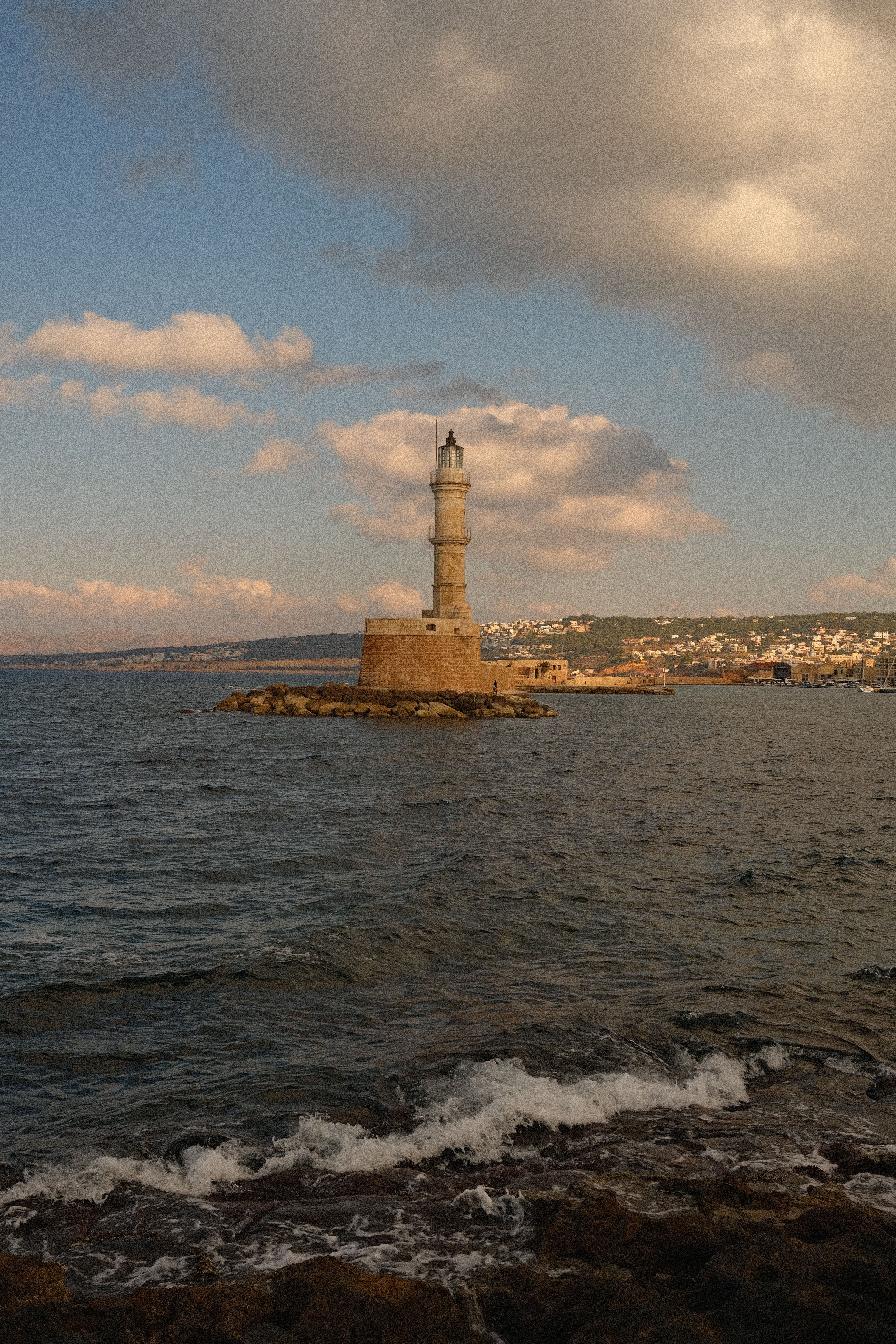 Capture the iconic Chania Lighthouse overlooking the Cretan Sea during a tranquil dusk setting with soft waves.