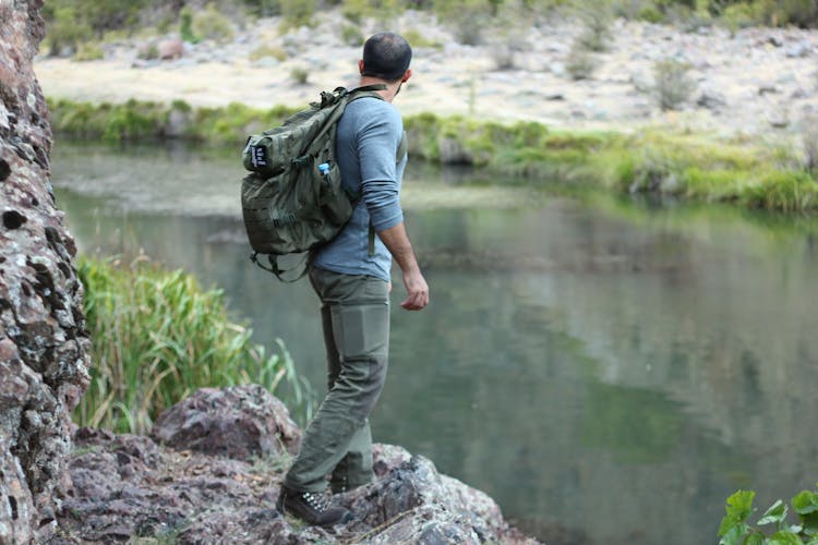 A Man In Gray Long Sleeves Standing On The Rock Near The River