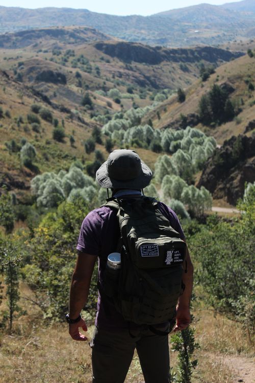 Free Man with a backpack and hat hiking through a stunning mountain vista in daylight. Stock Photo