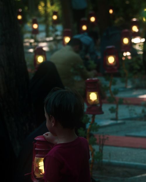 Free A child holding a glowing lantern in a serene Tehran garden at twilight, surrounded by dim lights. Stock Photo