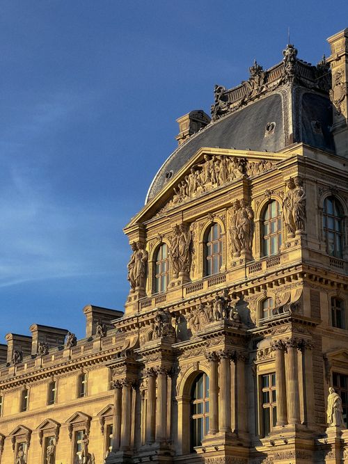 Free Elegant facade of the Louvre Museum in Paris against a blue sky. Stock Photo
