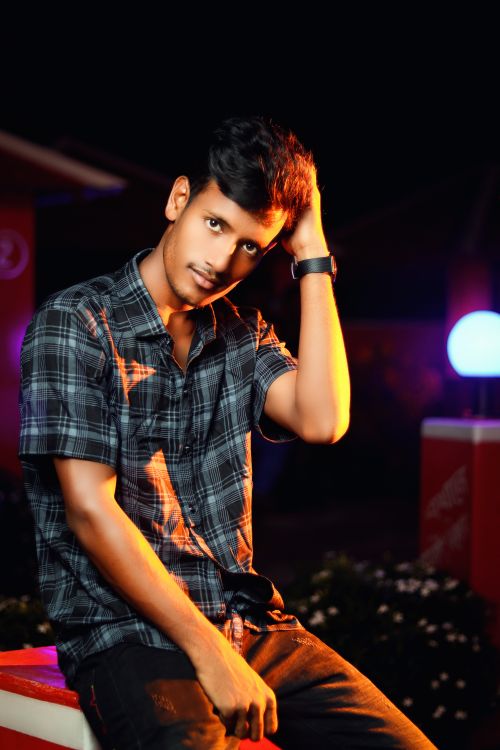 Free A young man in a checkered shirt sits outdoors, adjusting his hair and wearing a black wristwatch. Stock Photo