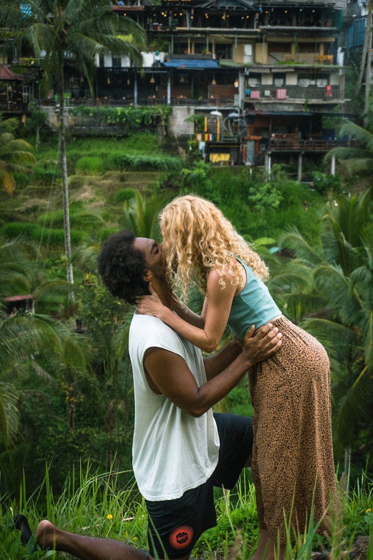 Woman Kissing Kneeling Man On River Bank