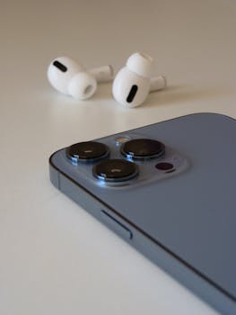 Close-up of a smartphone and wireless earbuds on a clean white surface, showing sleek design.