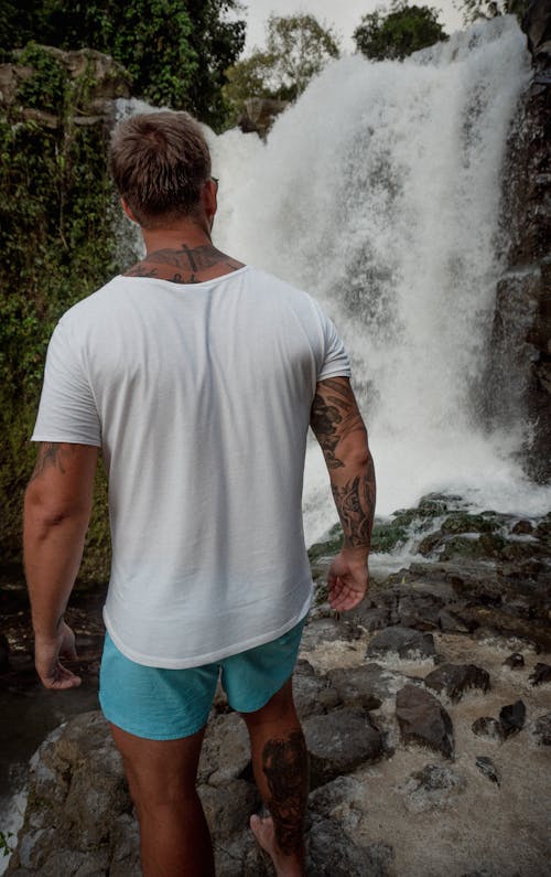 A Tattooed Man Standing Near a Waterfall