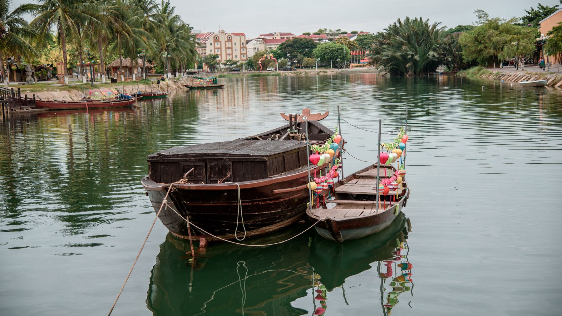 Charming view of traditional boats moored on a calm river in Hội An, Vietnam, surrounded by tropical scenery.