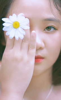 Close-up portrait of a woman holding a daisy on her eye, capturing elegance and natural beauty.
