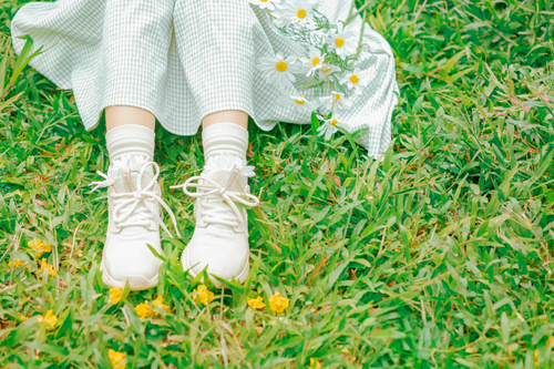 Free Close-up of child's legs in white sneakers resting on green grass with flowers. Stock Photo