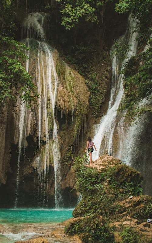 Person Standing on a Cliff Edge Near a Cascading Waterfalls