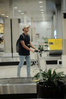 A young man pushes a luggage cart in an airport baggage claim area.