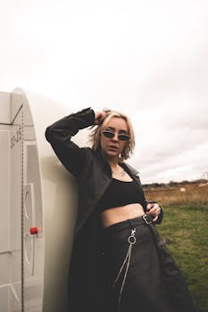 Fashionable woman posing in sunglasses and black coat outdoors, exuding confidence and style.