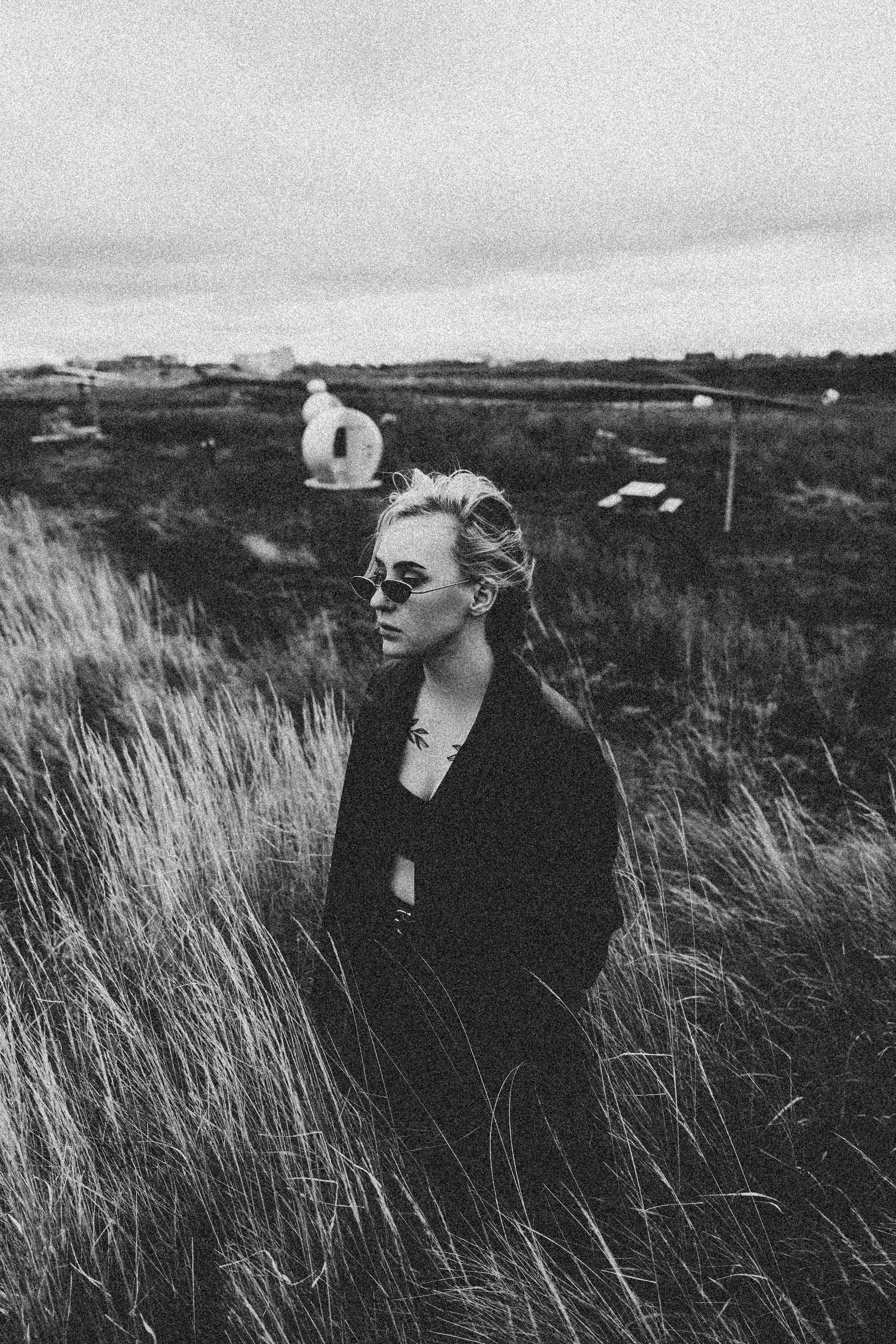 A Grayscale Photo of a Woman in Black Jacket Standing on Grass Field ...