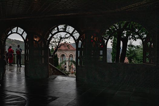 Rain-drenched castle terrace with arches revealing scenic views and visitors.
