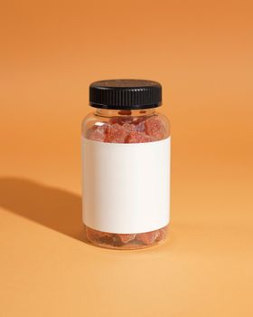 Close-up of a clear supplement bottle with gummies against an orange background.