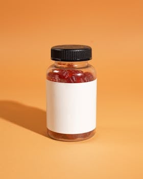 Clear bottle filled with red gummies on an orange background, perfect for supplement mockups.
